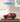 Red LEGO Ford Bronco SUV model in clear display case on wooden table, indoor setting