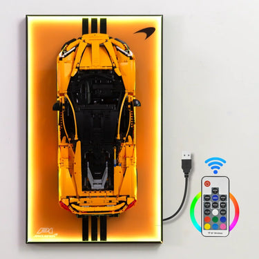 Yellow LEGO McLaren P1 model displayed on illuminated orange backboard with remote control and USB cable