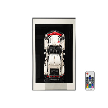 Framed white model Porsche 911 car with red roof and black base displayed on black background with remote control