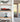 Red Formula 1 car model in display case on wooden shelf with potted plant and flower model below in modern room