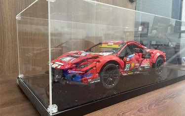 Red Ferrari model car displayed in a clear dustproof acrylic display case on a wood surface