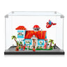 LEGO blue house with red roof, minifigures holding surfboards, palm trees, and flying spaceship in clear display case