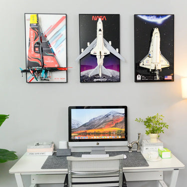 Modern white desk with iMac, books, plant, and wall-mounted LEGO models of a yacht and NASA space shuttles