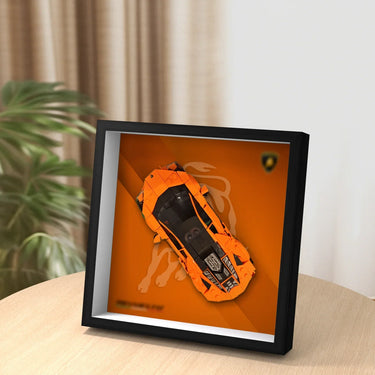 Framed LEGO Lamborghini model in orange displayed on a wooden table with blurred plant background