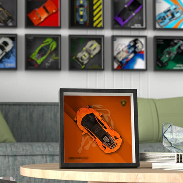 Orange Lamborghini model displayed in a black frame on a wooden table with car posters on the wall in a modern living room