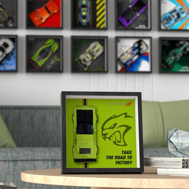 Framed Lego green muscle car model on a table with 'Take the Road to Victory' text and muscle car wall art in background