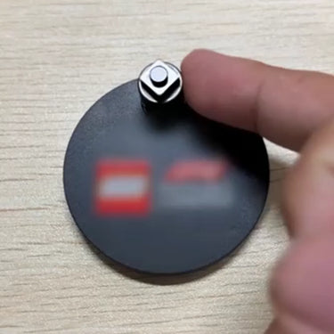 Hand adjusting a black circular camera lens cover with a silver screw on a wooden surface