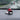 Red LEGO mini Formula 1 car model on a black round base on a car dashboard, rainy road visible through windshield