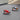 Two miniature red and blue toy racing cars with drivers on round black bases on car dashboard